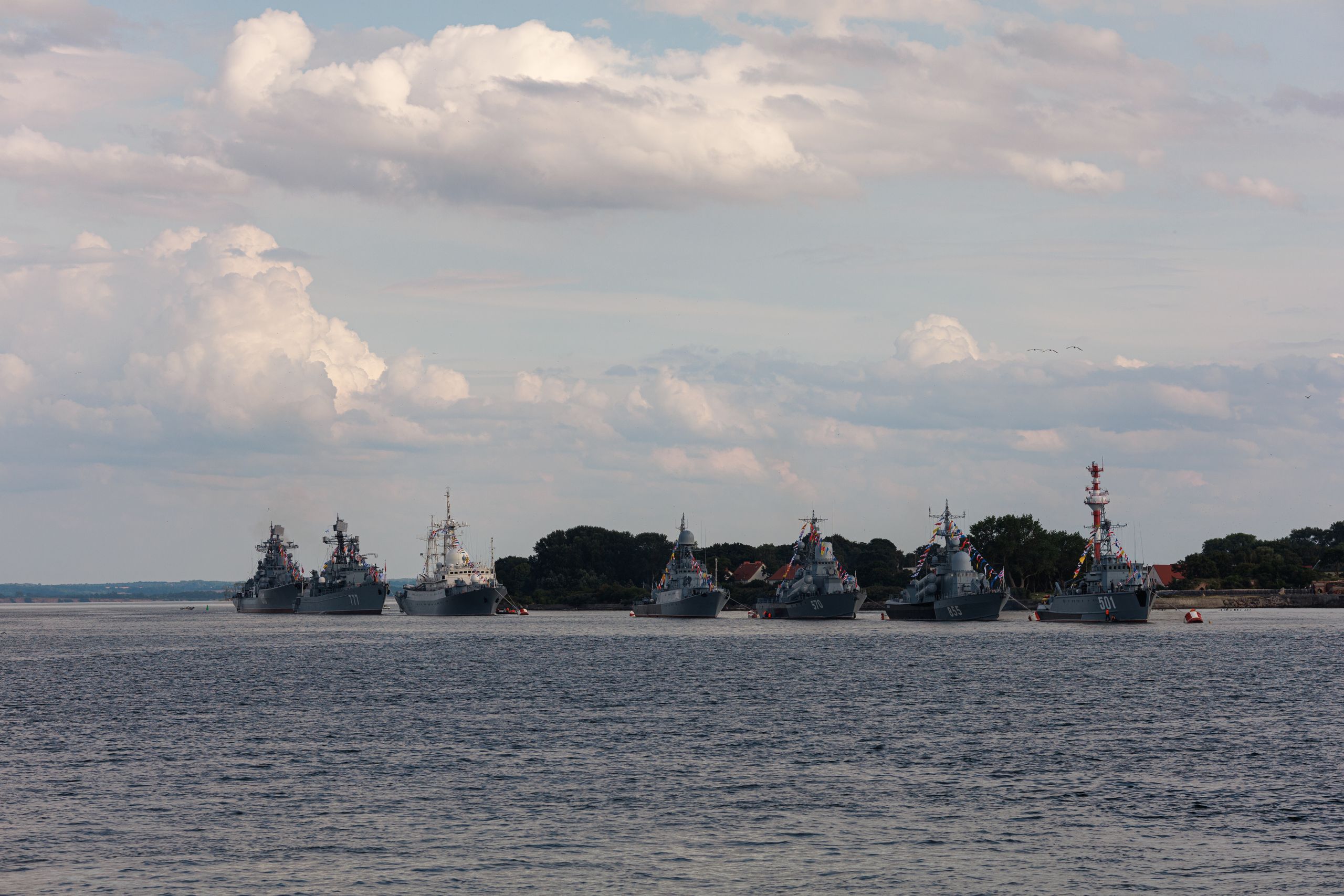A fleet of military ships anchored with a cloudy sky backdrop.